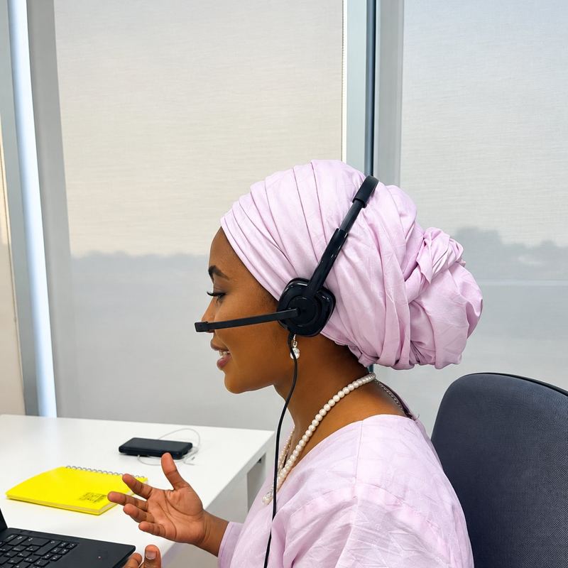 A woman in a pink headscarf wearing a headset at a help desk
