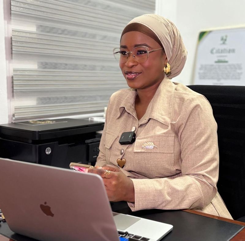 A professional woman in a beige jacket and headscarf working on a laptop