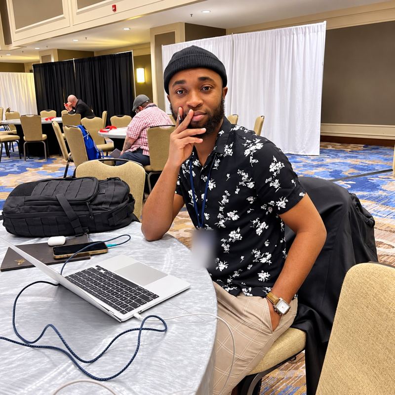 A young man in a patterned shirt working on a laptop at a conference table